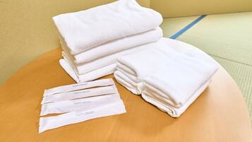 A stack of white towels and four individually wrapped items labeled "TOOTH BRUSH" on a wooden surface.