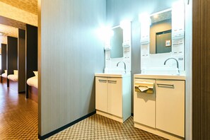 Bathroom features two sinks with mirrors, a towel dispenser, and a paper towel dispenser, set against a light-colored backdrop.