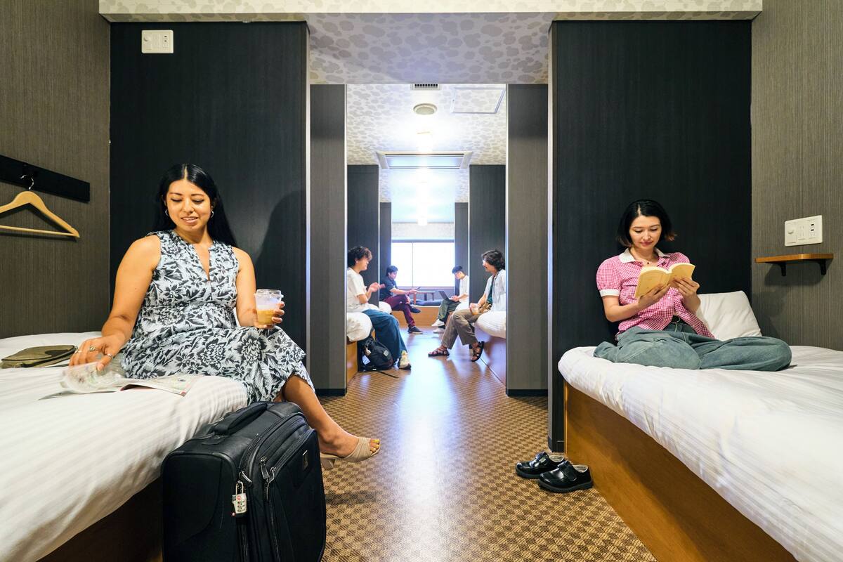 A hotel room with two beds, a suitcase, and a person reading a book.