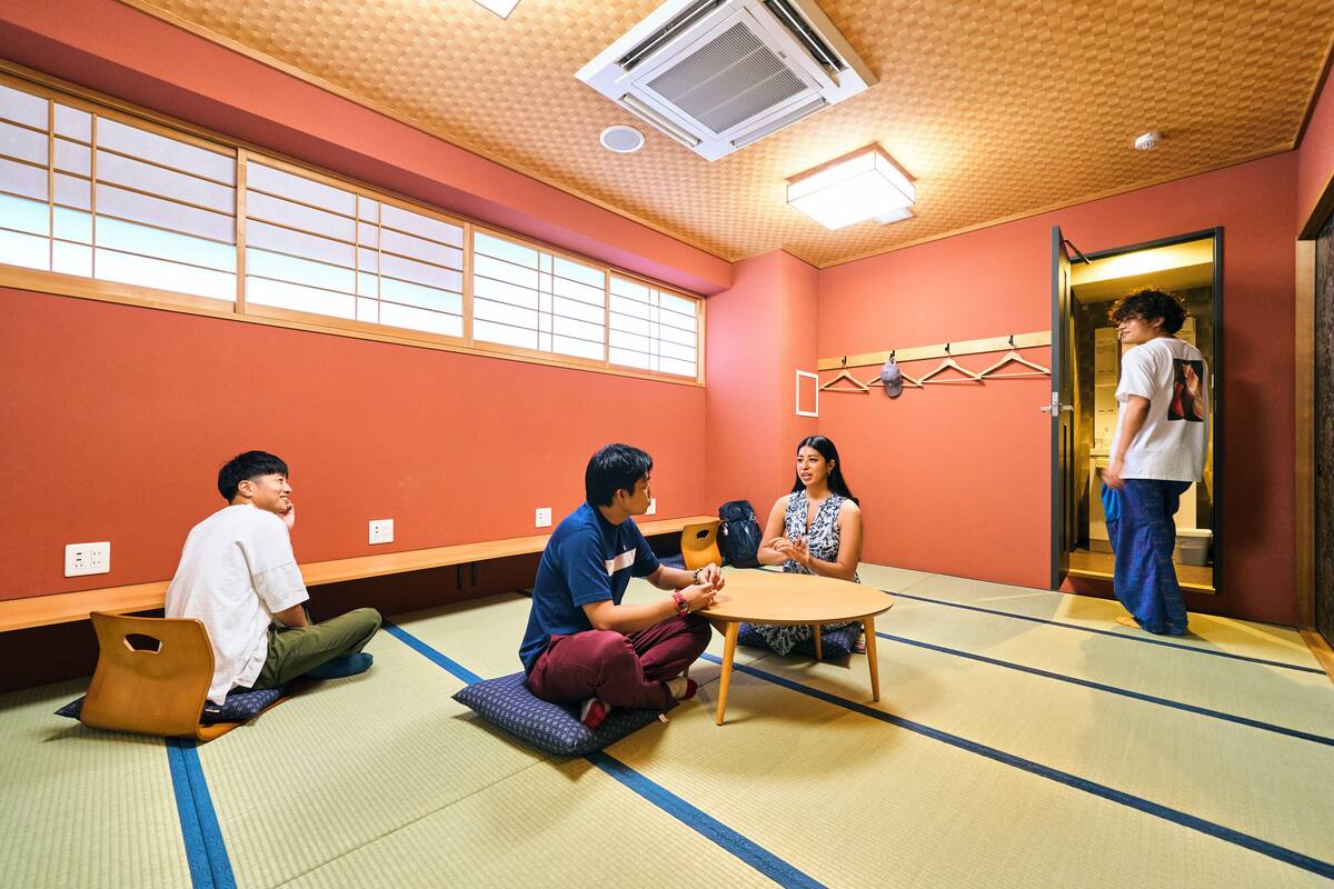 A tatami mat room with a low table, a sofa, and a person standing by a door.