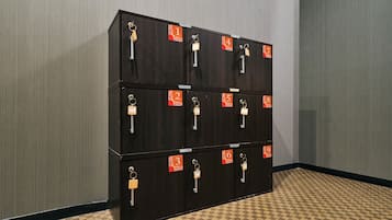 Una hilera de 12 taquillas de madera oscura con etiquetas numeradas, dispuestas en una esquina frente a una pared con textura.