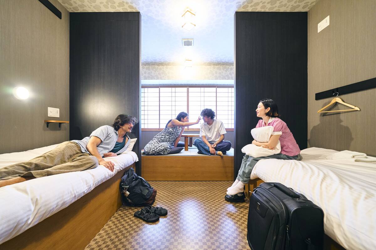 A dormitory room with four beds, a large window, and a hanging light fixture.