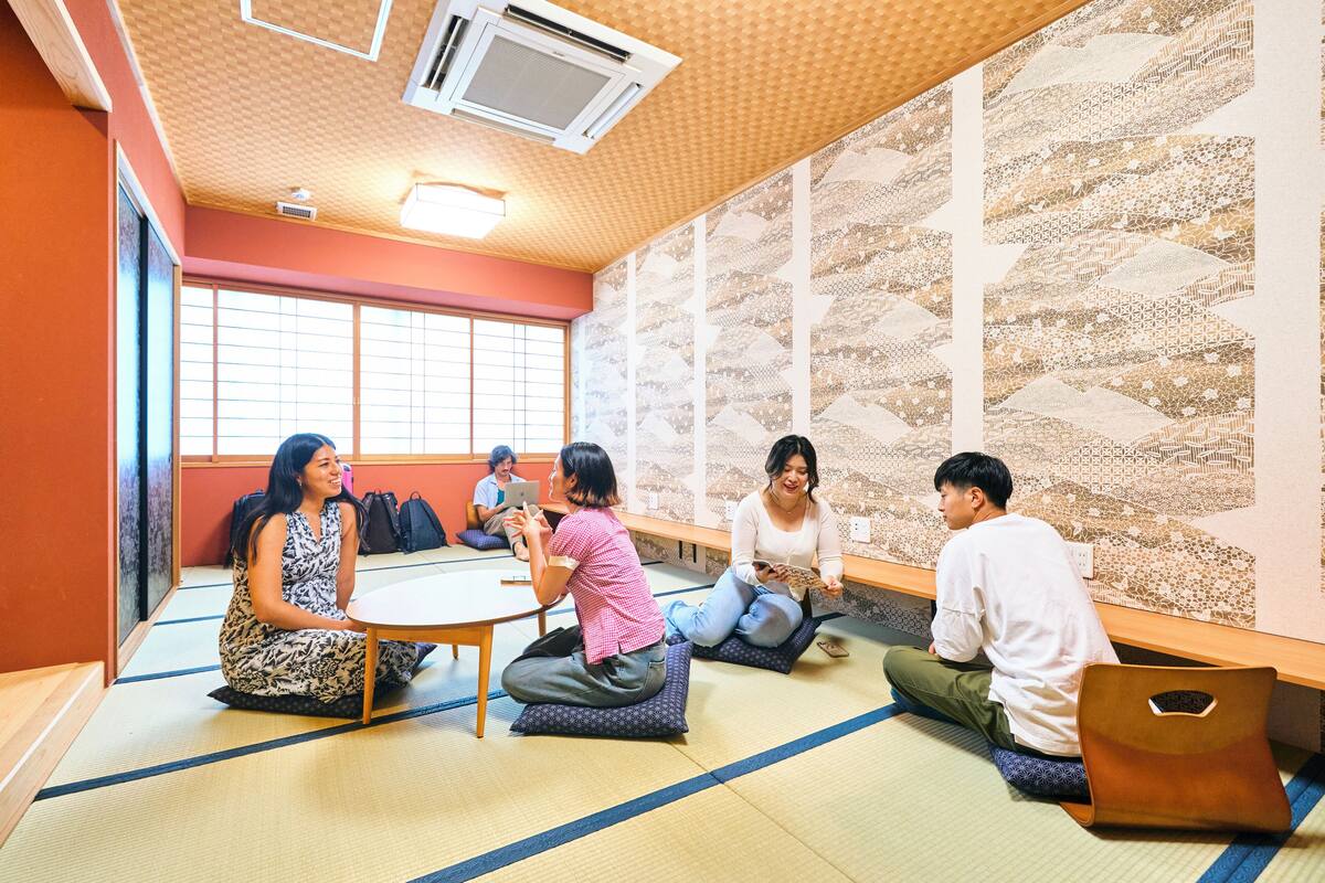 A tatami mat room with a low table, cushions, and a large patterned wall.
