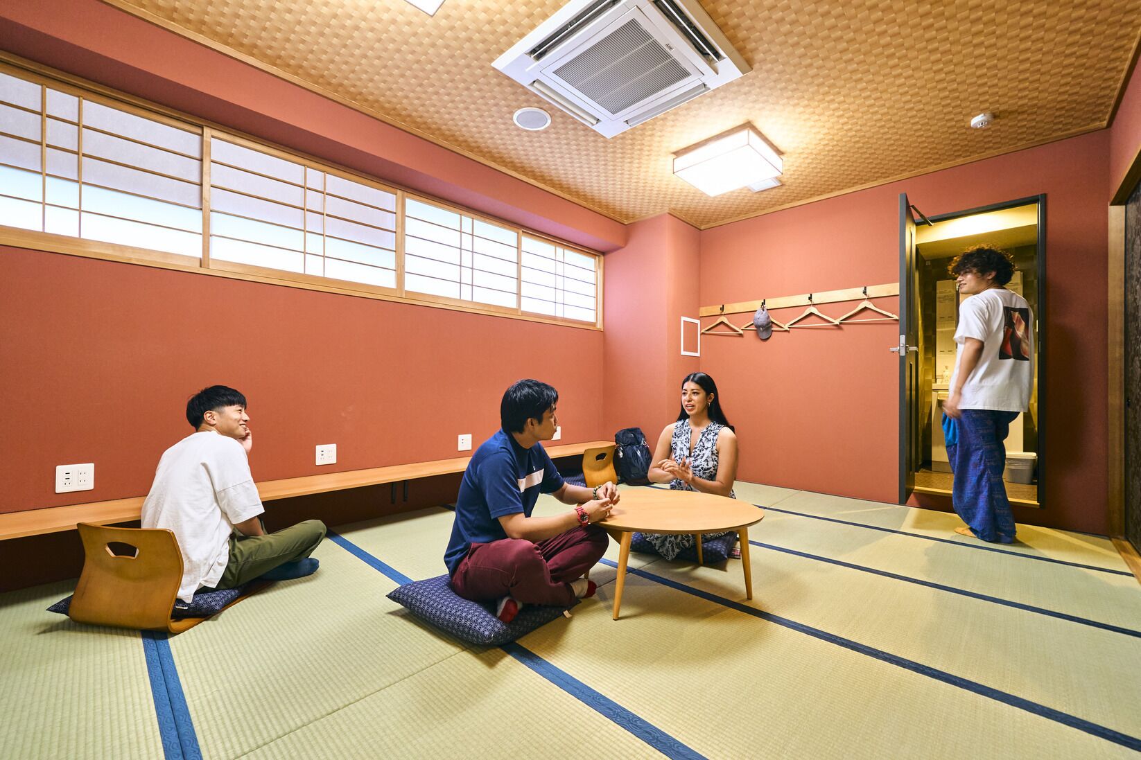 A tatami mat room with a tatami mat table, a wooden bench, a wall-mounted air conditioner, and a sliding door.