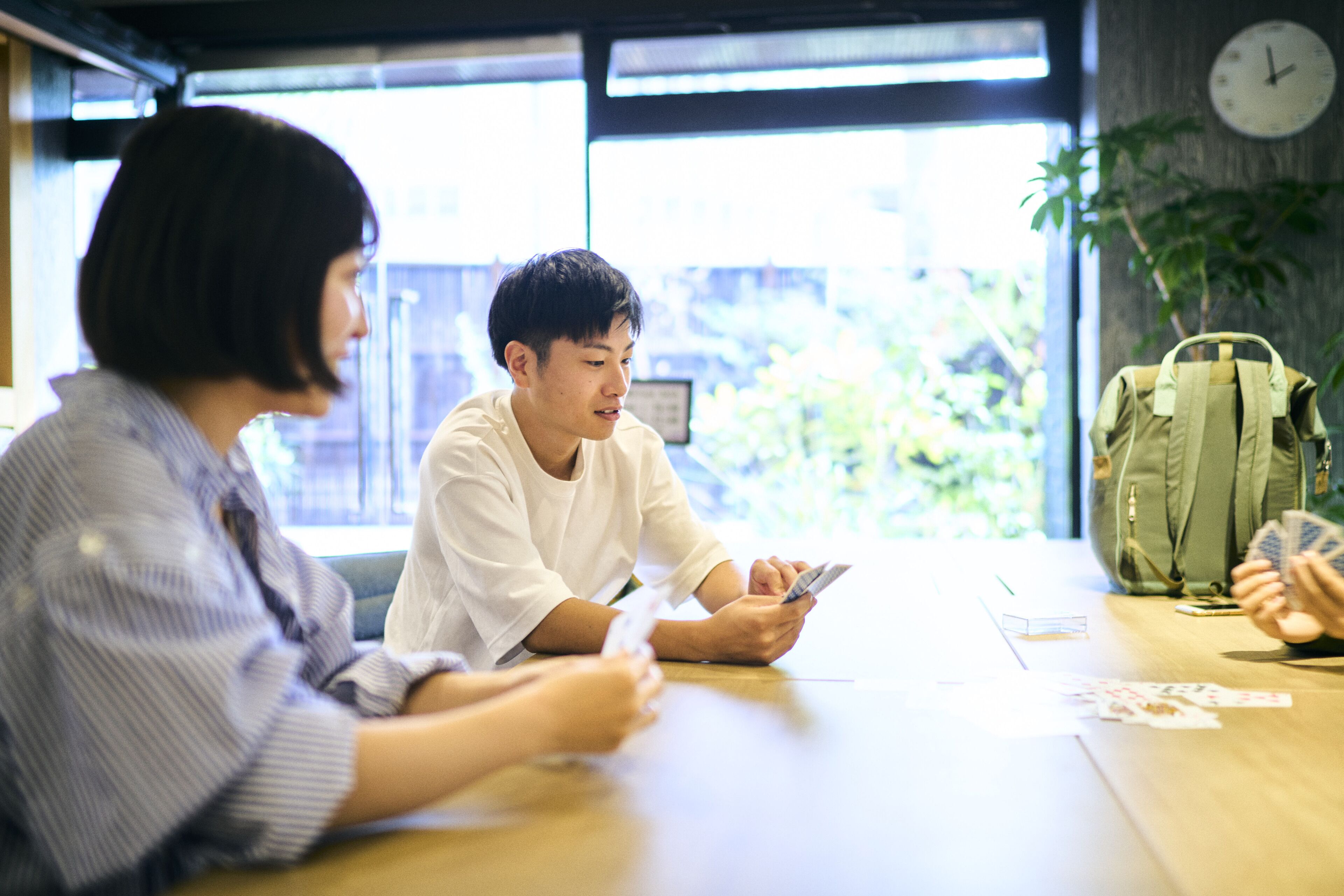 A group of people sitting at a table with a clock on the wall and a plant in the background.