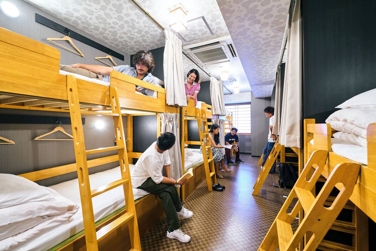A dormitory room with bunk beds, wooden furniture, and a patterned floor.