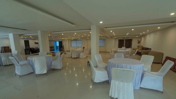 A spacious indoor area with multiple round tables and chairs, some covered with white tablecloths.