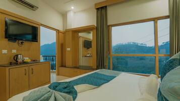 A hotel room with a bed, a TV, a window with a view of the mountains, and a kitchenette area.