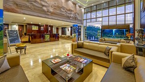 A spacious lobby with a reception desk, comfortable seating, a large aquarium, and a mural on the wall. - Excel Hotels & Resorts Bhimtal (Nainital)