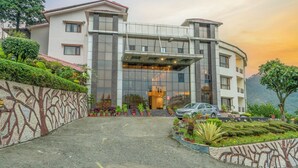 A modern building with a large glass entrance, surrounded by landscaped gardens and a decorative wall. - Excel Hotels & Resorts Bhimtal (Nainital)
