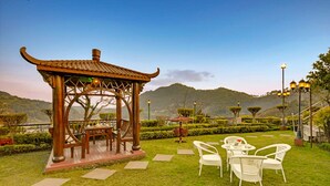 A gazebo with a traditional roof, surrounded by a well-maintained lawn and white chairs. - Excel Hotels & Resorts Bhimtal (Nainital)