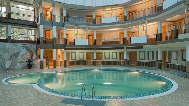 A multi-level atrium with a central swimming pool, balconies, and a glass ceiling. - Excel Hotels & Resorts Bhimtal (Nainital)