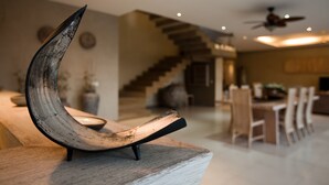 A modern interior with a unique crescent-shaped sculpture on a wooden table, a staircase leading to an upper level, and a dining area with chairs and a table. - Villa Seminyak 3 Bedroom (Seminyak)