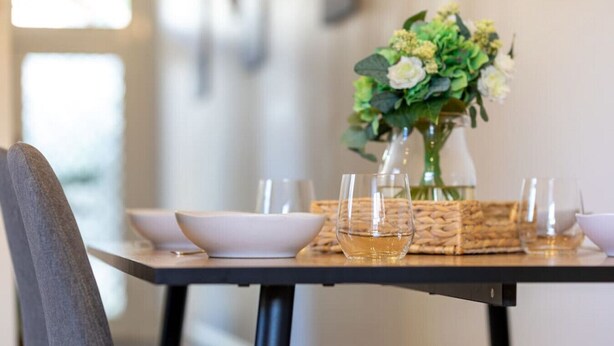 A dining table set with white plates, bowls, and glasses, accompanied by a vase of flowers.