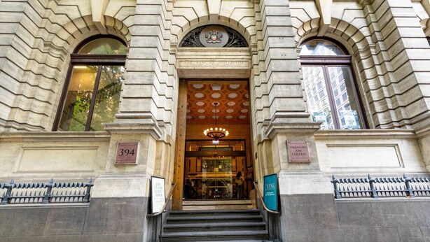 A building entrance with a large arched doorway, a coat of arms above, and a sign reading "TREASURY ON COULONS". - Elegance and heritage stay - CBD (Melbourne)