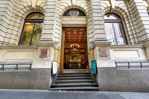 A building entrance with a large arched doorway, a coat of arms above, and a sign reading "TREASURY ON COULONS". - Elegance and heritage stay - CBD (Melbourne)