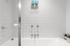 Een moderne badkamer met een douchecabine van glas, een wit bad en een klein plankje met toiletartikelen.