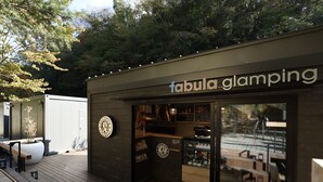 Ein moderner Außenbereich zum Sitzen mit einer Holzterrasse, einer Glasfassade und einem Schild mit der Aufschrift 'fabula glamping'.