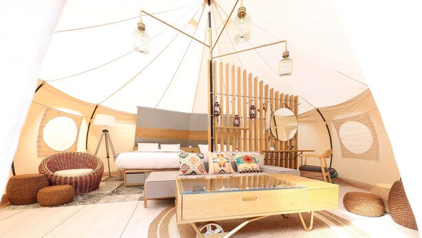 Ein Zelttyp-Zimmer mit einem Bett, einem Glastisch, Korbmöbeln und einer Hängelampe.