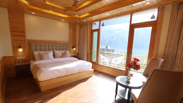 A wooden-paneled bedroom with a large bed, a small table with a vase, and a chair. - Golden Wood Manali By Rosetum (Manali)