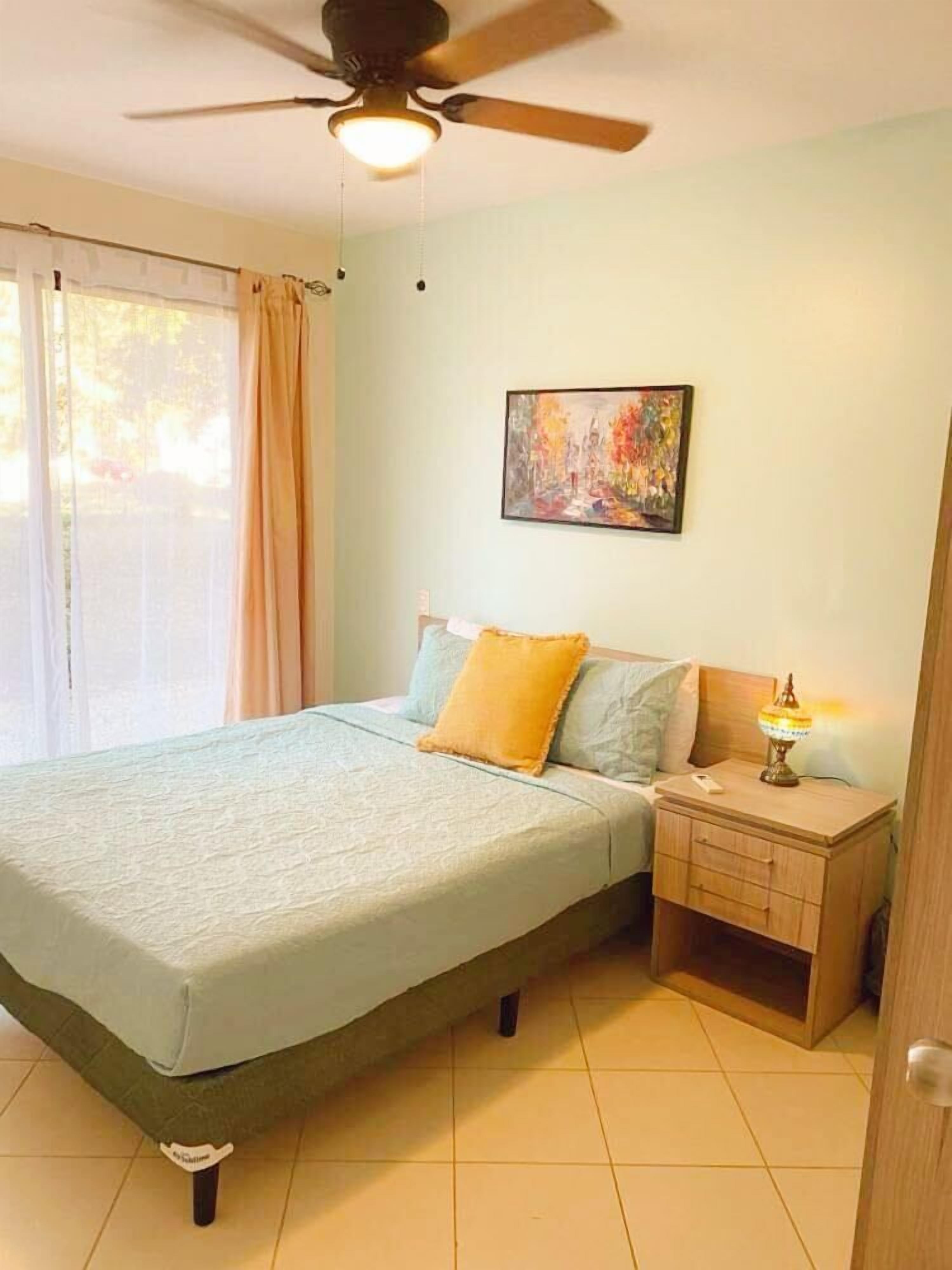 Un dormitorio con cama, mesita de noche y ventilador de techo.