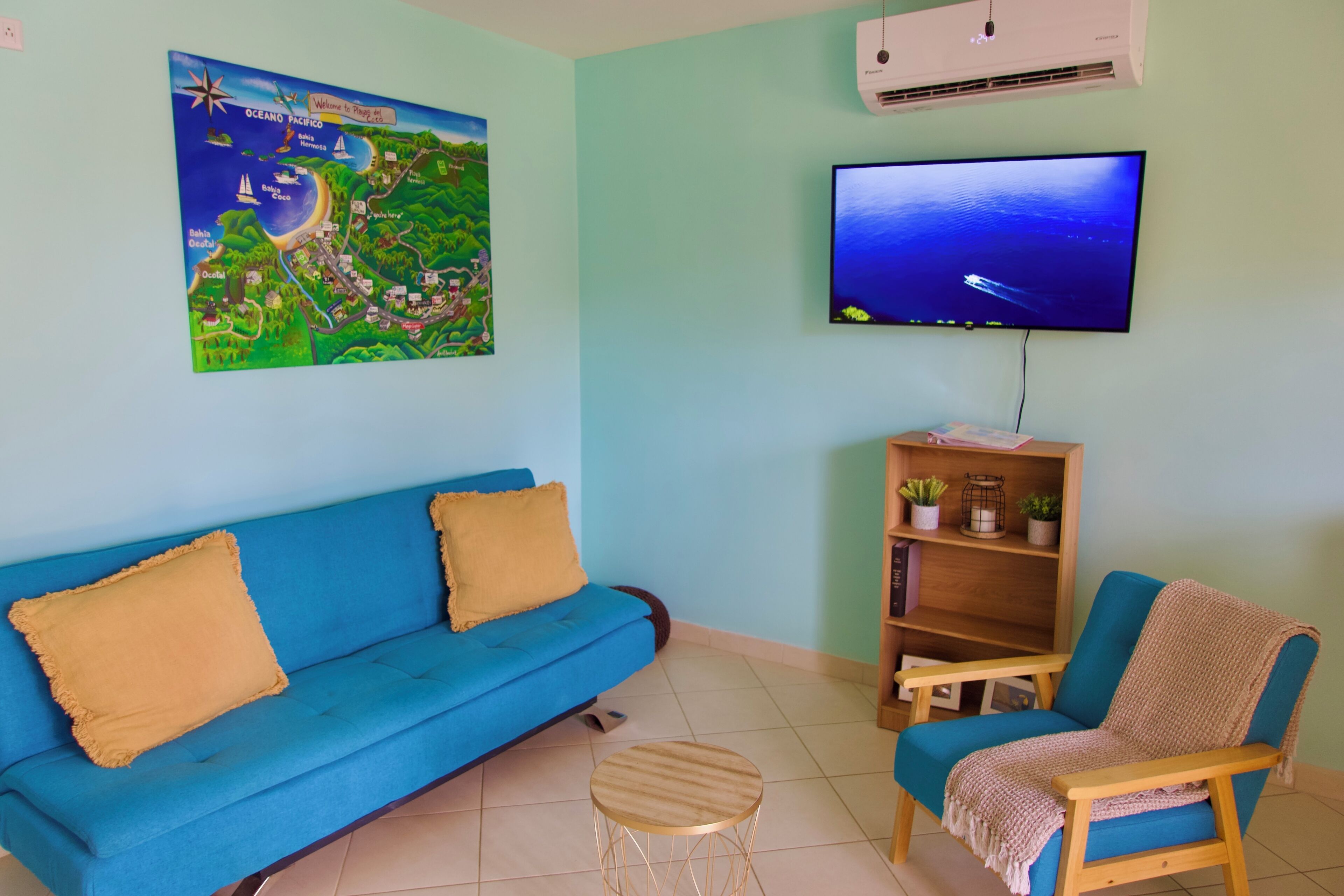 A living room with a blue sofa, a wooden chair, a small round table, a television, and a map on the wall.