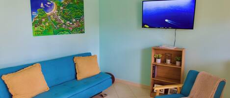A living room with a blue sofa, a wooden chair, a small round table, a television, and a map on the wall.