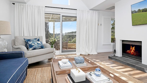 A spacious living room with a large window, a fireplace, and a sofa with striped cushions.