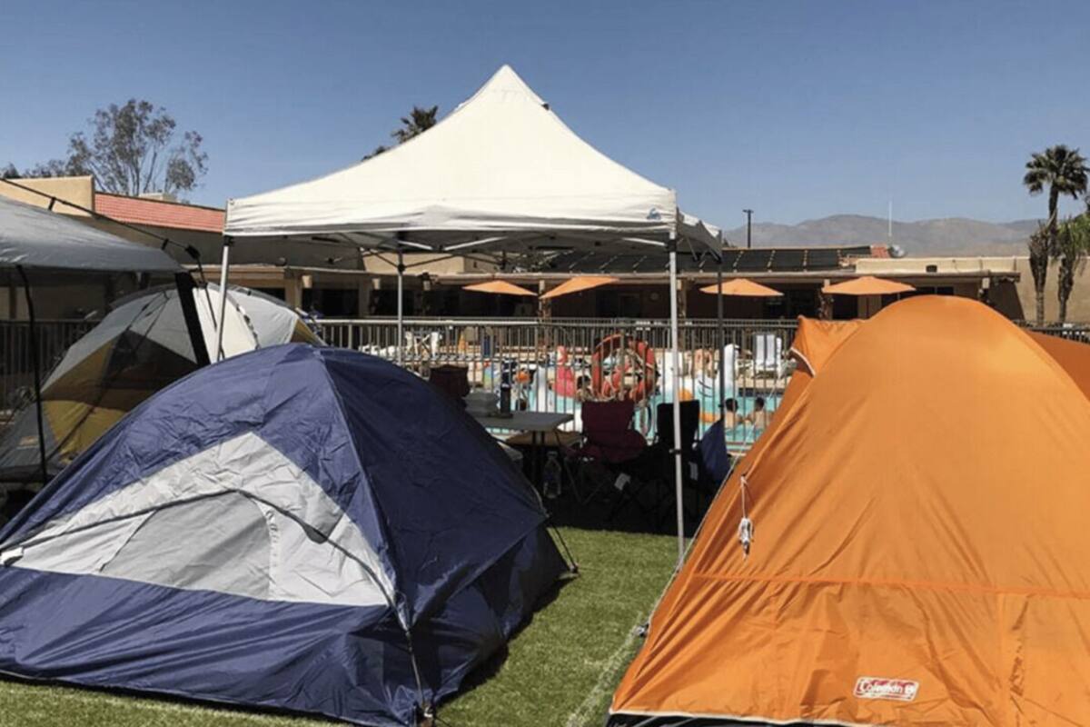 Zona de camping con tiendas de campaña y una estructura tipo toldo blanca.