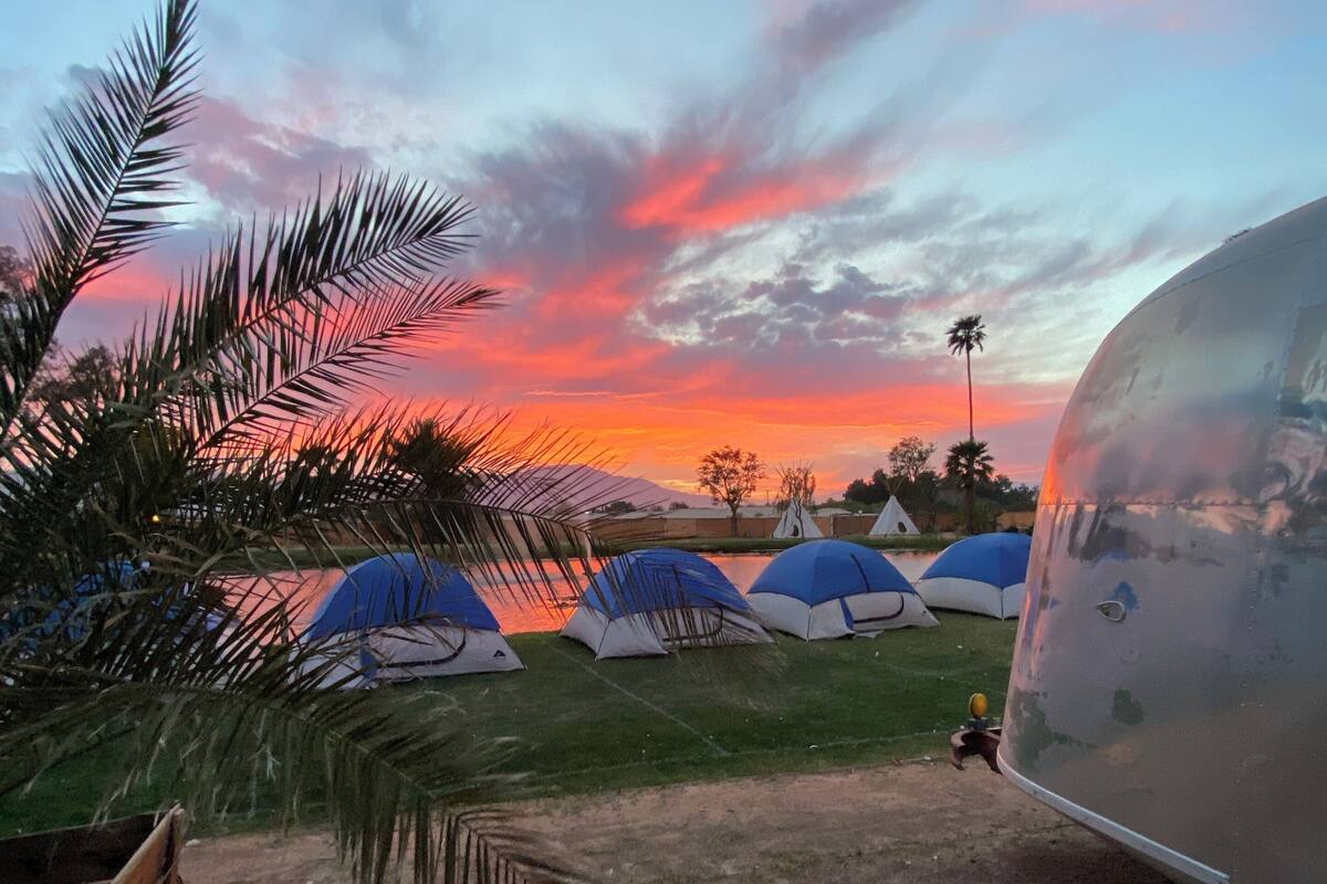 Un camping con varias tiendas de campaña y una gran estructura esférica, probablemente una cúpula geodésica, al atardecer.