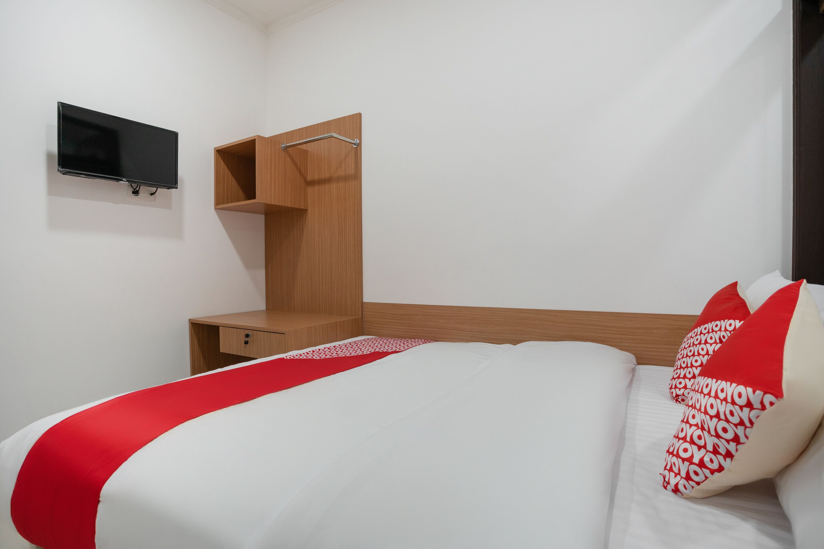 Una camera d'albergo con un letto, una TV fissata al muro e un mobile contenitore in legno.