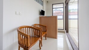 Un espace d’accueil avec un comptoir en bois, deux chaises en bois, un téléviseur à écran plat et une vue sur un toit recouvert de tuiles, visible à travers une porte vitrée.