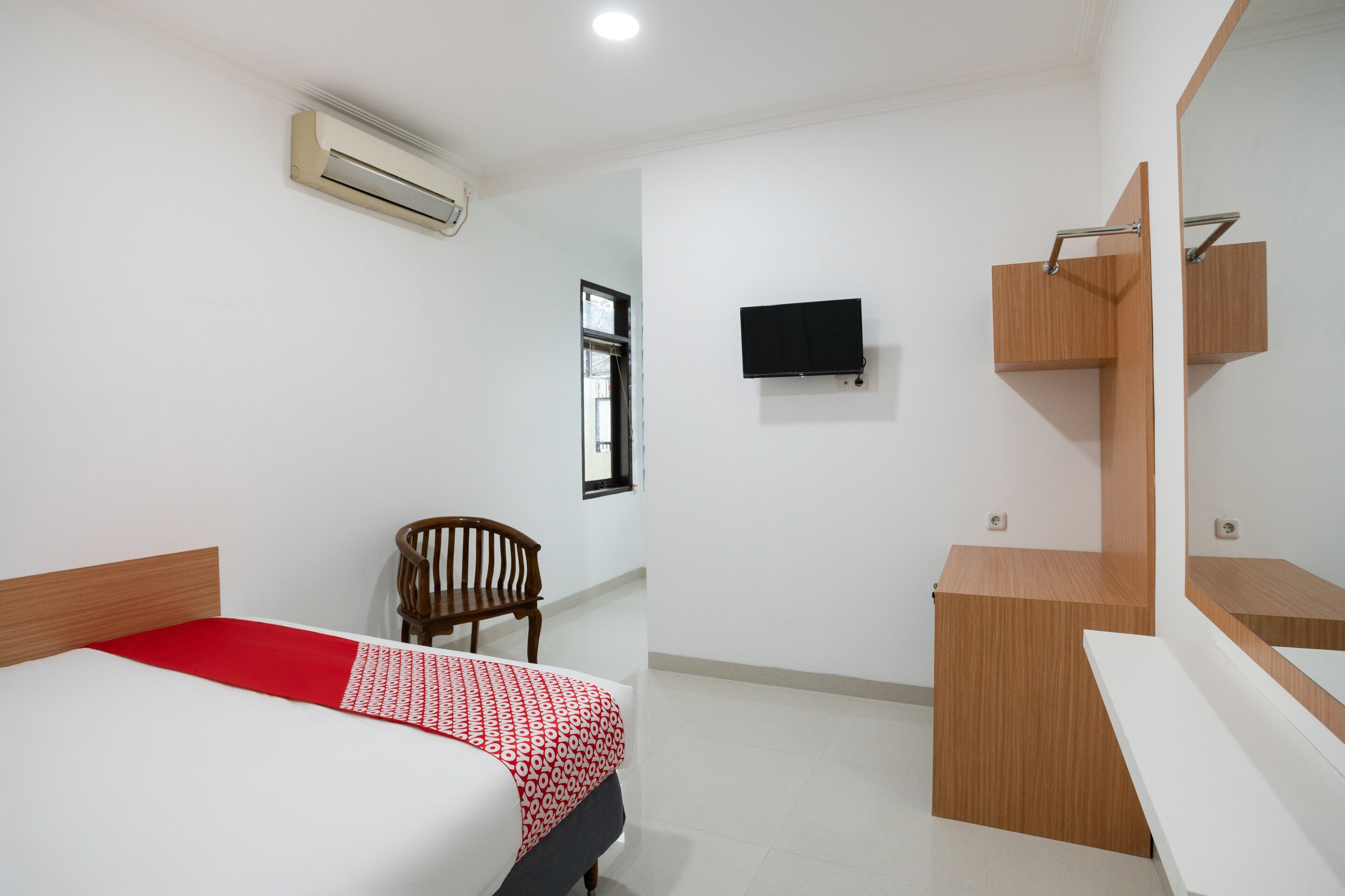 A hotel room with a bed, a chair, a desk, a television, and an air conditioning unit.