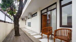 Un couloir avec un arbre, deux bancs en bois et une porte avec une fenêtre.
