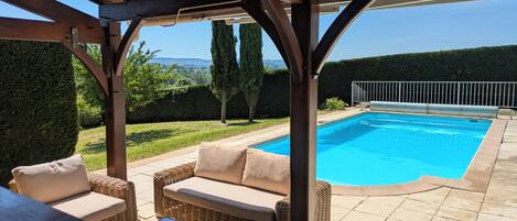 Un espace extérieur abrité, doté d’une piscine, de meubles en osier et offrant une vue sur le paysage.
