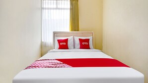 Ein Bett mit weißer und roter Bettwäsche, zwei Kissen mit dem Schriftzug "OYO", eine rot-weiße Steppdecke und ein Fenster mit weißen Vorhängen und einem gelben Vorhang.