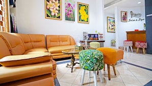 Ein modernes Wohnzimmer mit einer Couch, einem Hocker und einem kleinen Tisch. An der Wand befinden sich gerahmte Blumenbilder und ein Schild für 'Pohita Salon & Spa'.