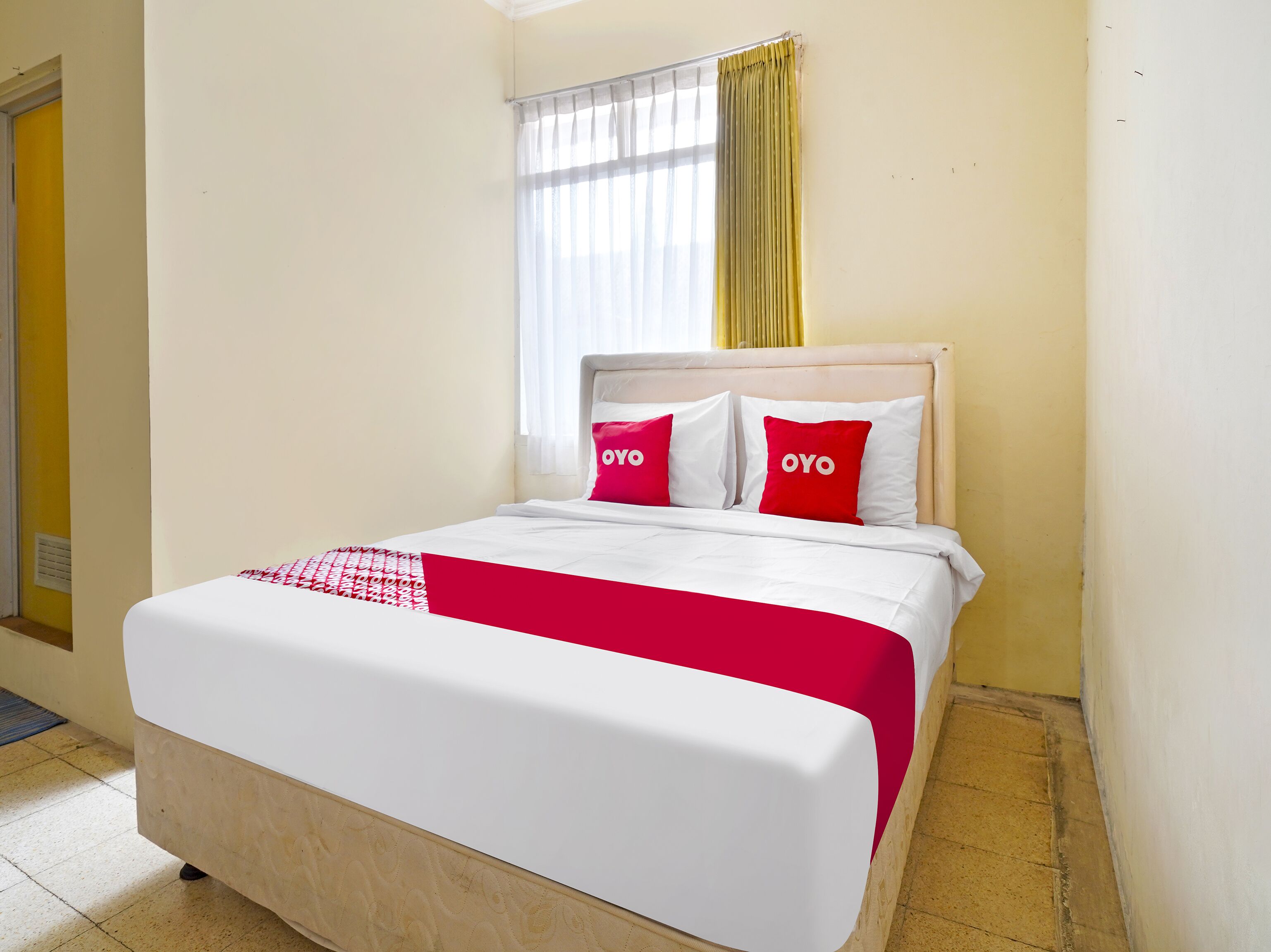 Une chambre d’hôtel avec un lit, une fenêtre avec des rideaux jaunes et une porte.