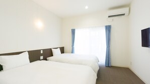 Une chambre d’hôtel avec deux lits, une fenêtre avec des rideaux, un appareil de climatisation et un téléviseur à écran plat fixé au mur.