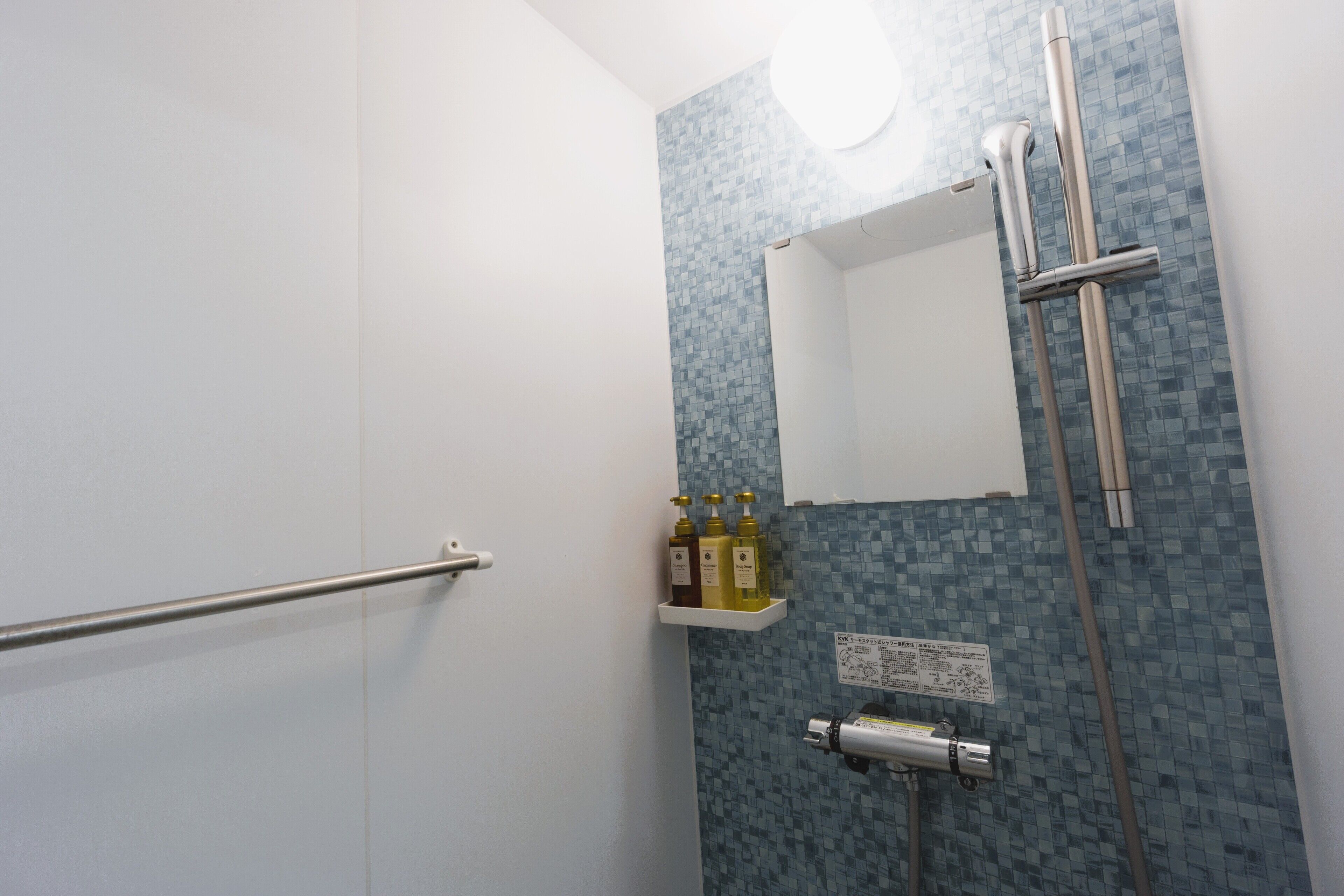A bathroom with a white door, a shower with a glass door, a shelf with toiletries, and a wall-mounted towel rack.
