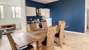 Une cuisine moderne avec des meubles blancs, un mur d’accent bleu et un coin repas comprenant une table en bois et des chaises en osier.