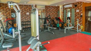A gym with various exercise equipment, a red carpet, and a brick wall. - Four Leaf Hotel (Budaun)
