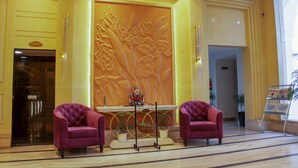 A lobby with two purple armchairs, a reception desk, and a large floral wall. - Four Leaf Hotel (Budaun)