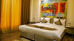 A hotel room with a large bed, a nightstand, a painting on the wall, and a window with curtains. - Four Leaf Hotel (Budaun)