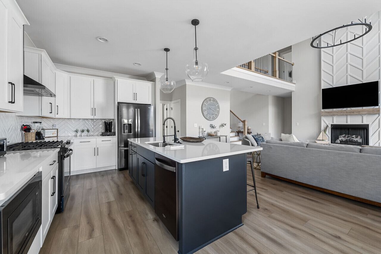 A modern kitchen with white cabinets, a central island, stainless steel appliances, and pendant lighting.