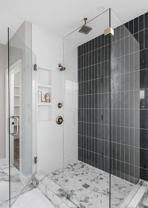 A modern bathroom with a glass-enclosed shower, black tiled walls, and a marble floor.