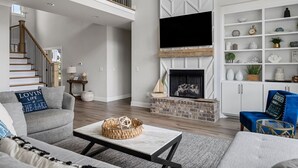 A modern living room with a fireplace, a flat-screen TV mounted above it, and a staircase leading to an upper level. - Beautiful Lake Home Retreat with Lake and Marina Access and Golf Cart (Winchester)