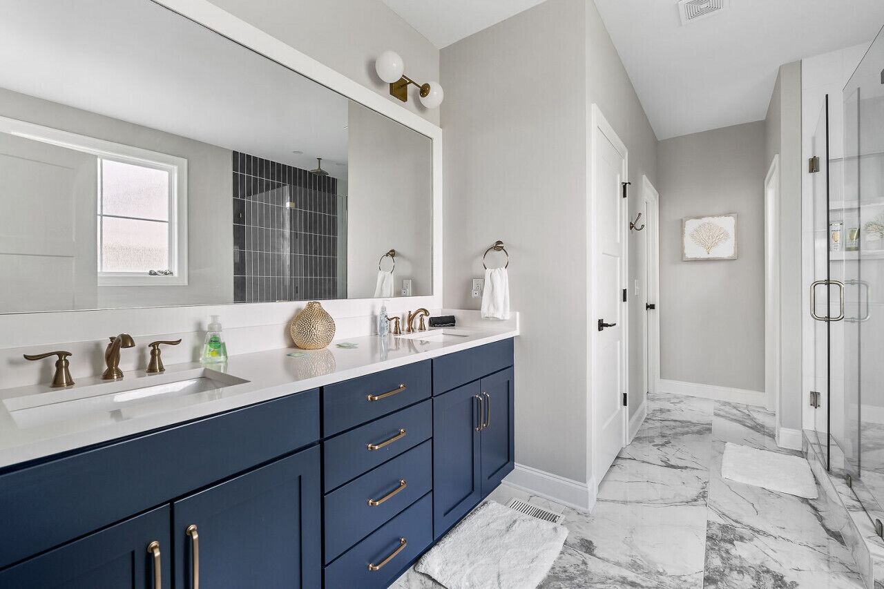 A modern bathroom with a large mirror, two sinks, and a walk-in shower.