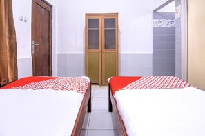 Une chambre avec deux lits simples, une armoire en bois et une porte donnant sur une salle de bain.