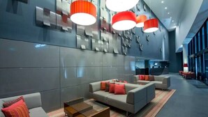 Un hall d’entrée moderne avec des canapés gris, une table basse et des lampes rouges.